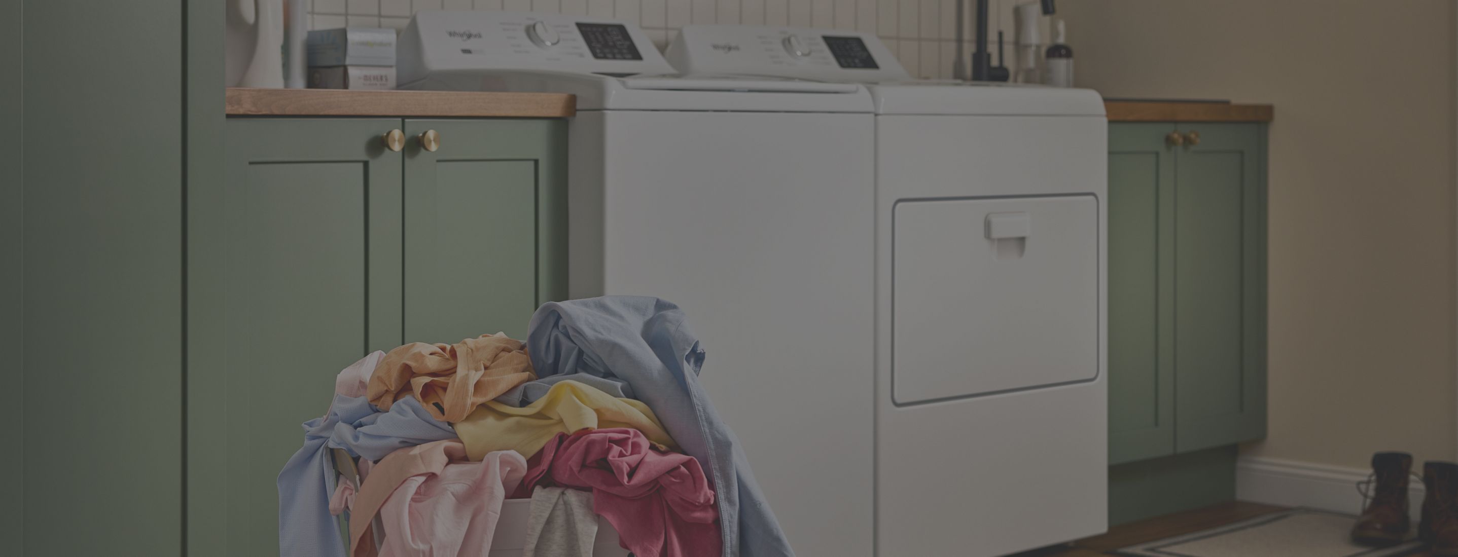 A person loads laundry in a Whirlpool® Top Load Washer and Dryer set