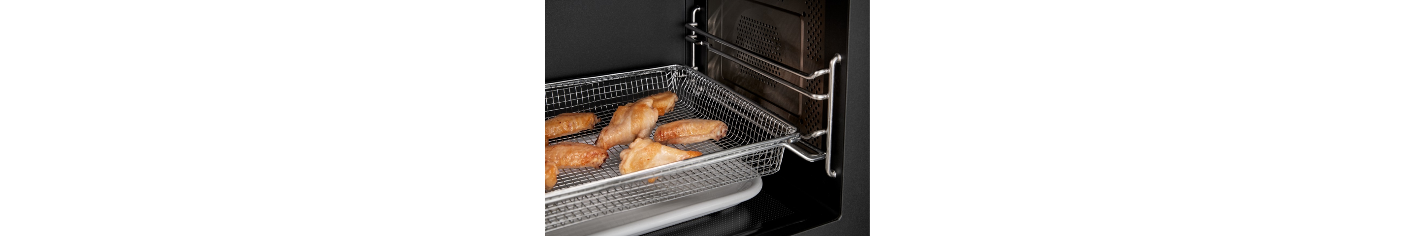 The inside of a microwave with chicken wings in the air fry basket.