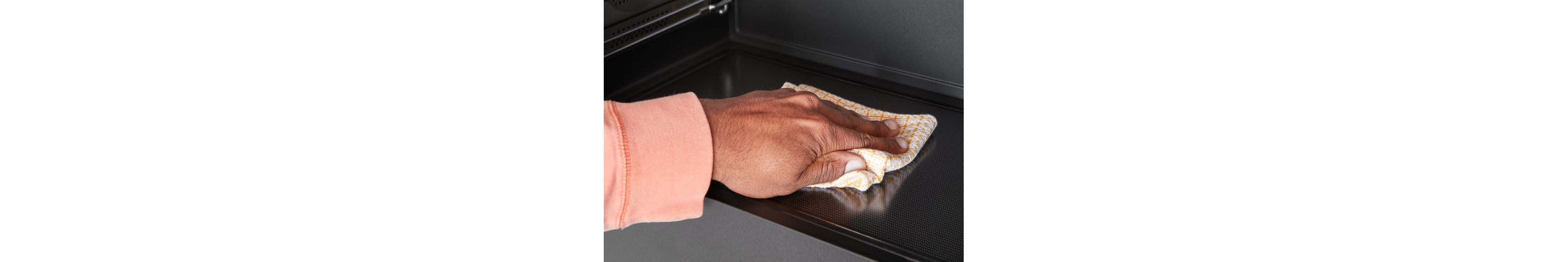 A person wipes the inside of a microwave with a cloth.
