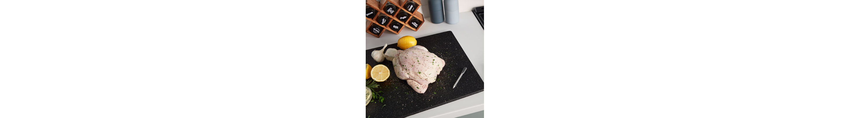 Whole raw chicken on black cutting board with ingredients