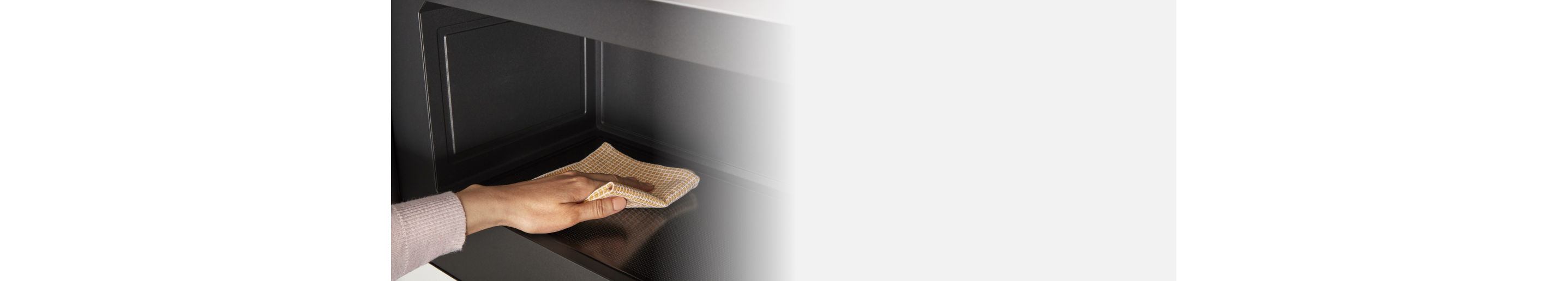 Person cleaning the interior of a microwave with a cloth