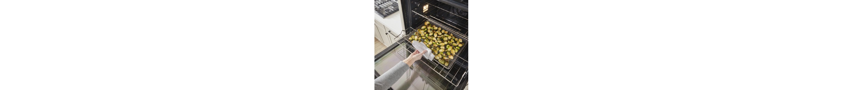A person removing a tray of roasted vegetables from an oven