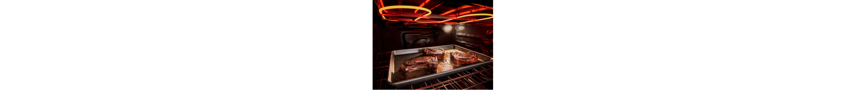 The inside of an oven with a pan of meat in it and the broiler coils lit up