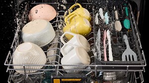 Third rack of a dishwasher with bowls, mugs and utensils mid wash