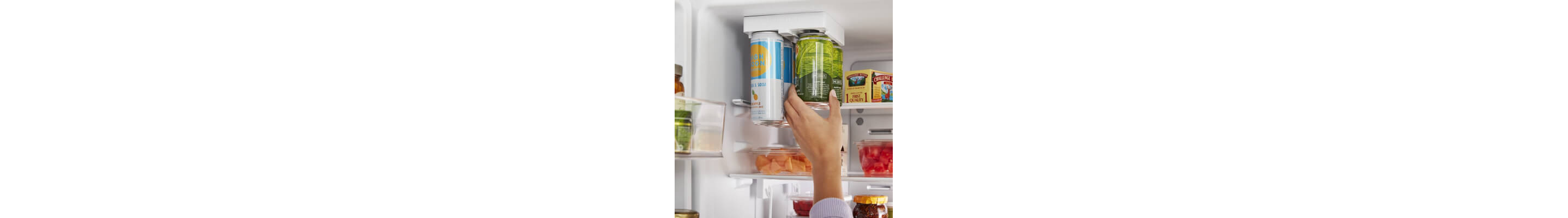 Person reaching for a canned beverage inside a refrigerator