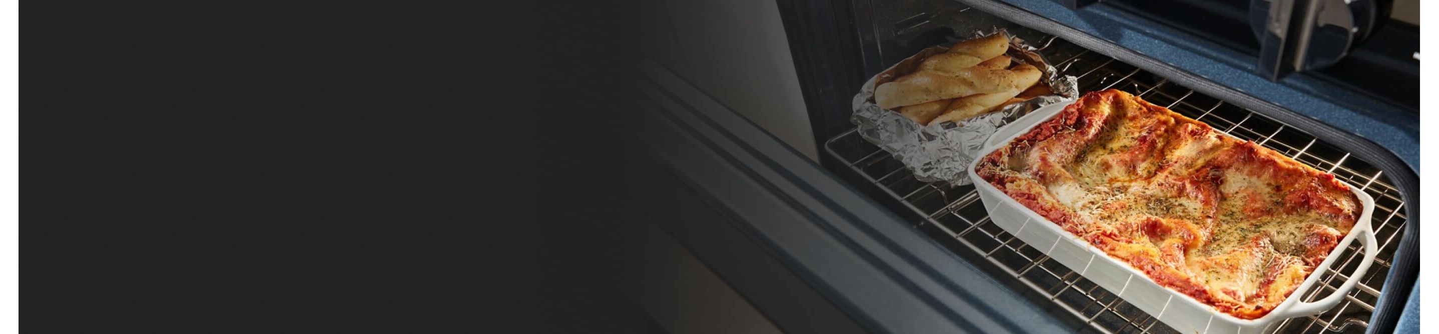 A lasagna and long rolls on a rack in the oven
