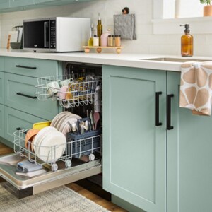 An open loaded dishwasher next to the sink surrounded by mint green cabinets