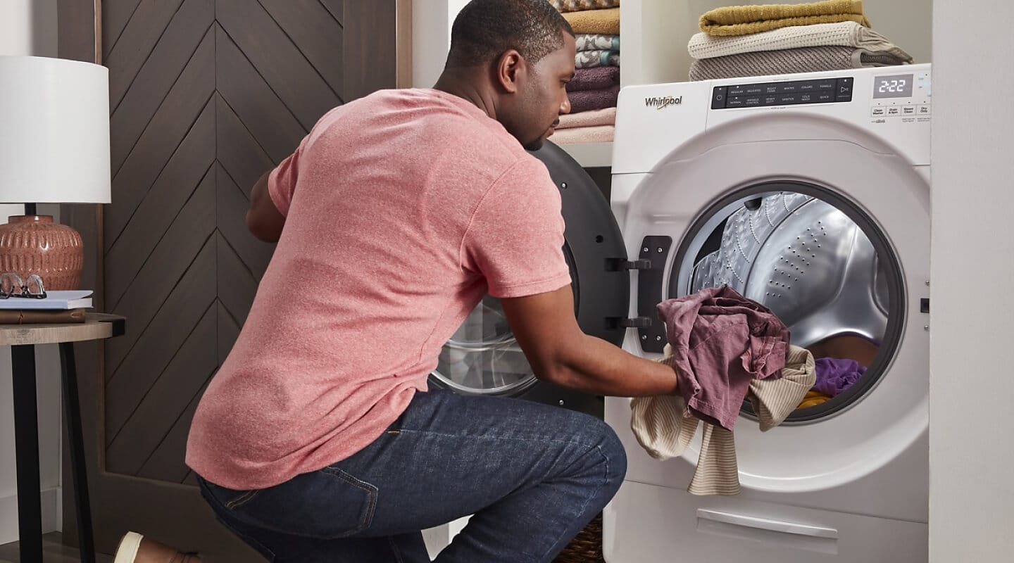 Person loading laundry into a white Whirlpool® Front Load Washer