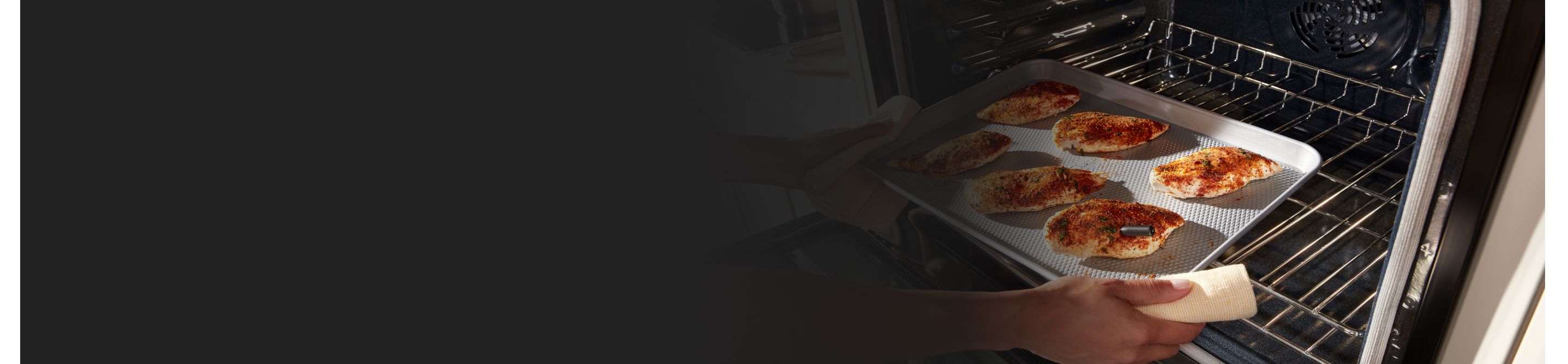 Person pulling spiced chicken breasts from an oven