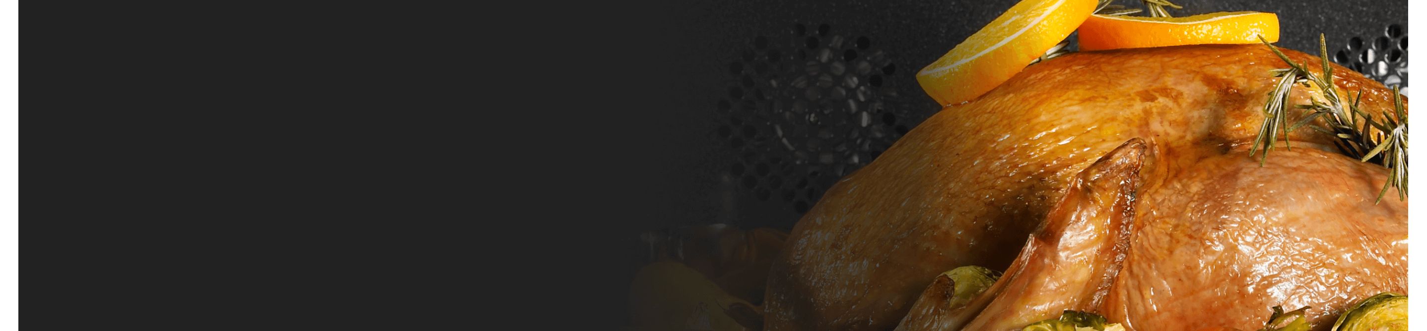 A turkey cooking in an oven garnished in rosemary and orange slices