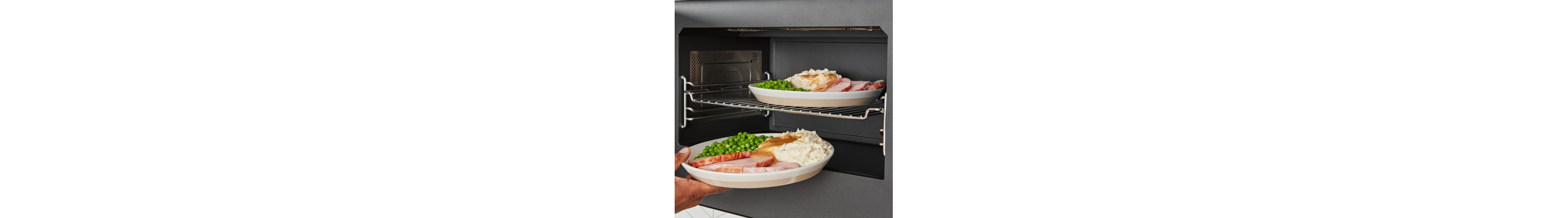 Person placing plates of ham, peas and mashed potatoes into a microwave