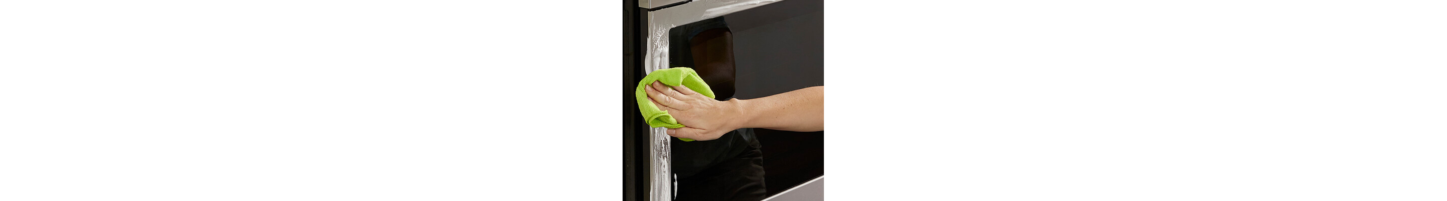 Person wiping oven’s stainless steel perimeter with green rag and cleaner