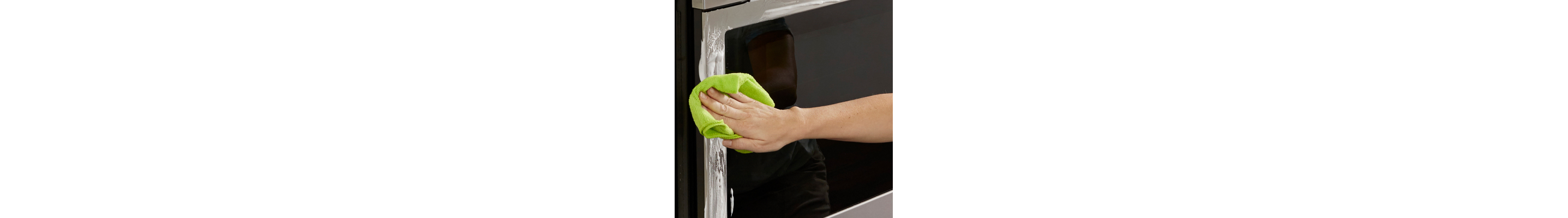 Person wiping oven’s stainless steel perimeter with green rag and cleaner