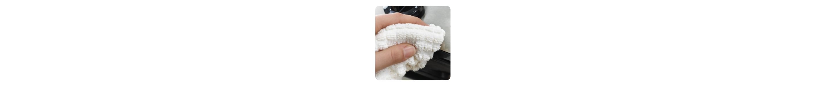 Close up of a hand using a towel to clean a stainless steel appliance 