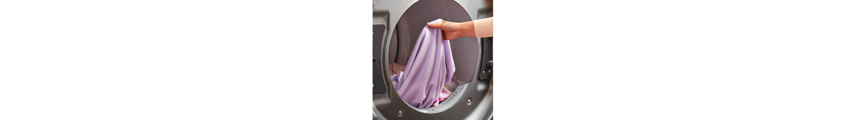 A hand holding a purple linen in the drum of a front load washer