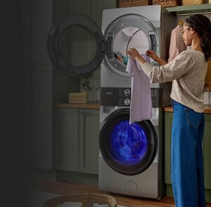 A person holding up a white shirt next to a stacked washer and dryer