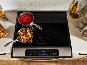 A pan of tomato sauce and a pan of vegetables heating on an induction cooktop