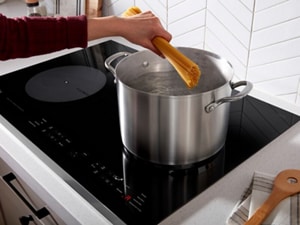A person dropping pasta into a pot of boiling water on an induction cooktop