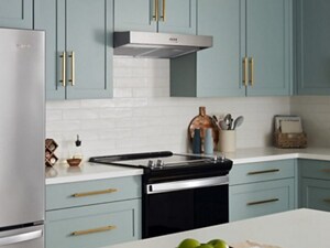 A kitchen with white counters and walls, blue cabinets, and a range hood over a range
