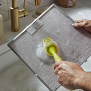 Someone cleaning a metal filter in a sink filled with soap