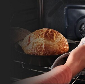 A person pulling fresh bread out of an oven 