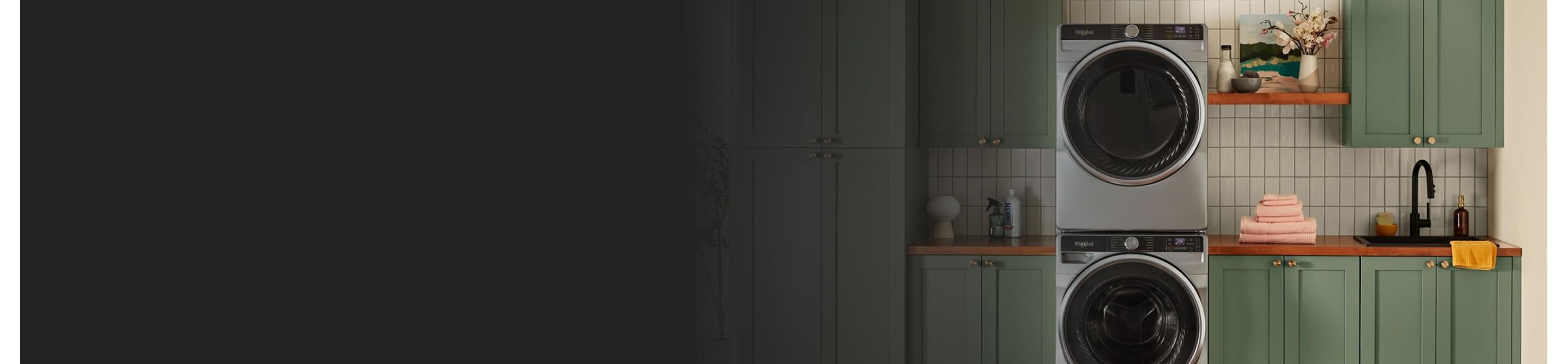 A stainless steel stackable washer and dryer in a laundry room with green cabinetry