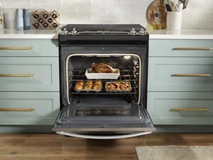 An oven with an open door showing a roast chicken and other sides