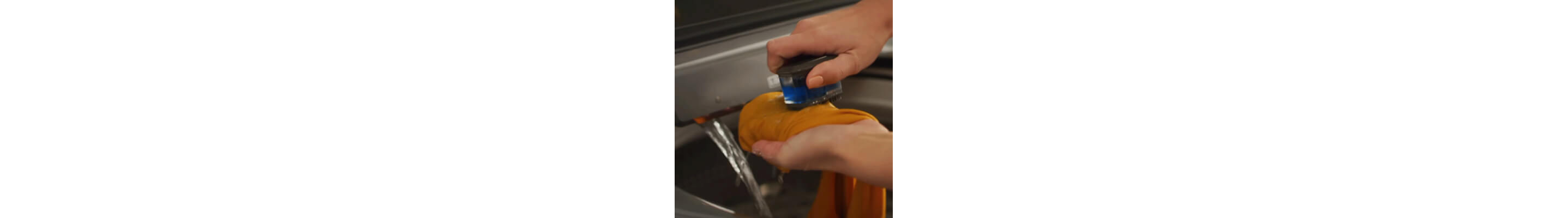 Close up of a person using a pretreat brush to spot treat odor on a garment
