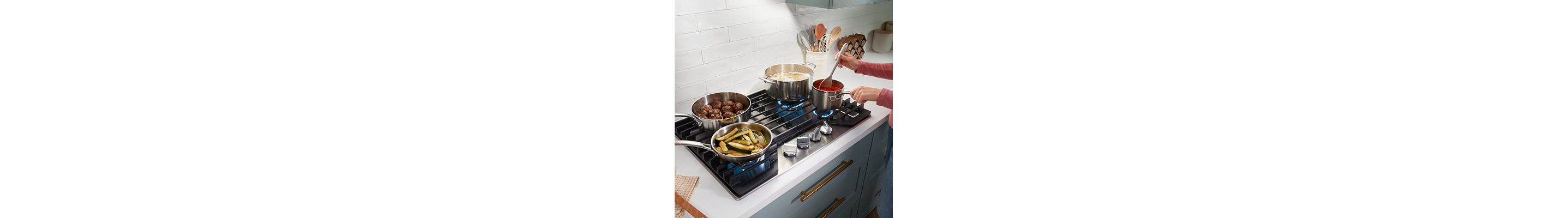Four dishes cooking on edge-to-edge grates of gas cooktop