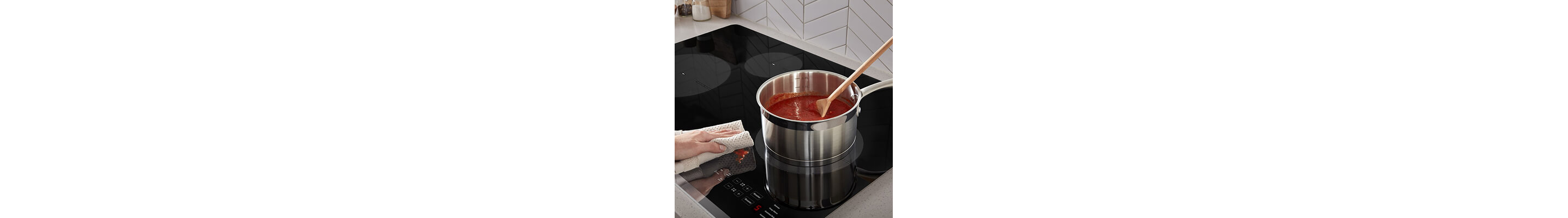 Person wiping spaghetti sauce splatter from ceramic glass cooktop surface