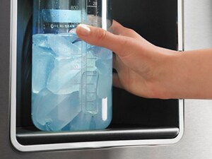 A person filling up a container with ice at a fridge dispenser