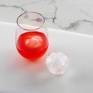 Ball ice on tray and in a glass with red beverage