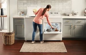 A person removing laundry from a Whirlpool® Top Load Washer and putting items into a Whirlpool® Dryer