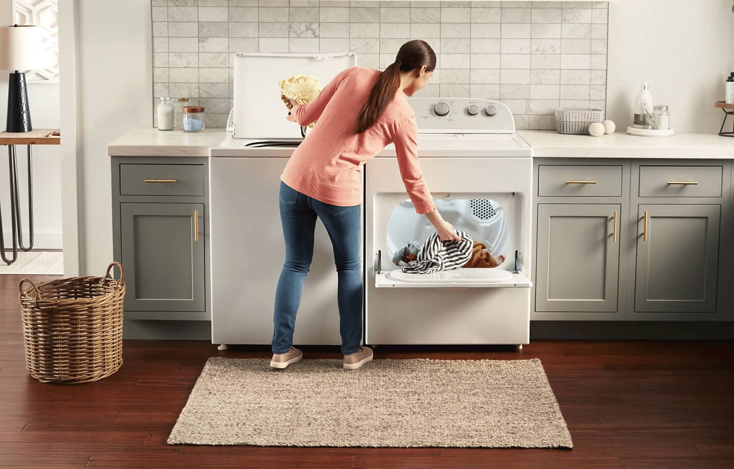 A person removing laundry from a Whirlpool® Top Load Washer and putting items into a Whirlpool® Dryer