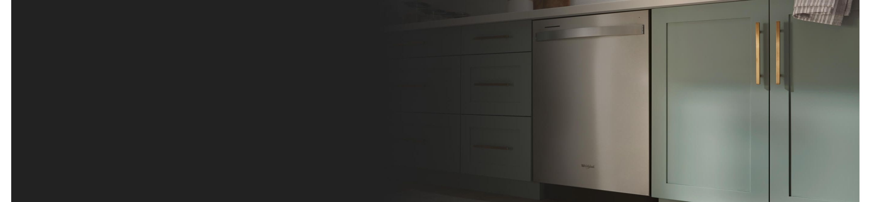 A Whirlpool® Built-In Dishwasher with Top Control and a towel handle placed between green cabinets and under white countertops