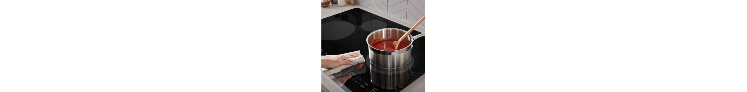 A hand wiping up sauce spilled on a Whirlpool® Induction Cooktop