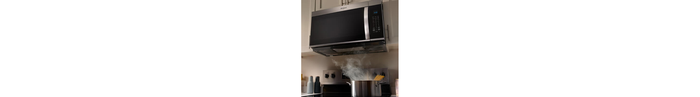 A pot releasing steam as it cooks on a stovetop below a microwave