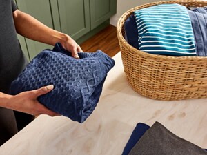Person holding a folded navy sweater next to a basket of folded clothes