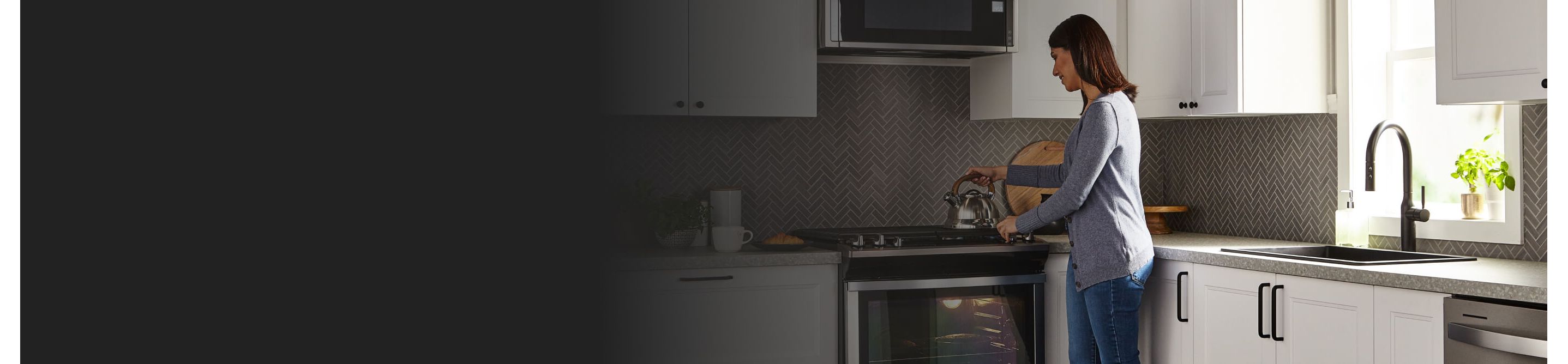 Person standing over a gas range with a hand on a tea kettle that’s resting on a stovetop in a kitchen with white cabinetry