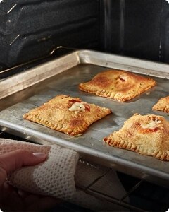 A person pulling a tray of food out of a Whirlpool® Range