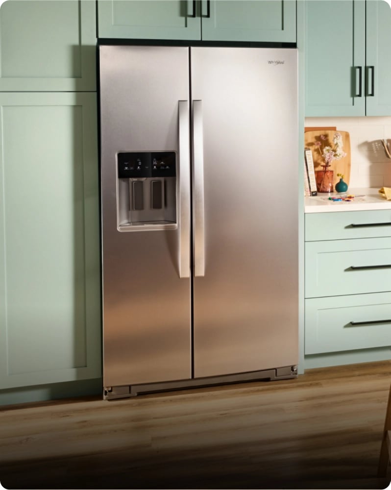 A stainless steel refrigerator installed between light green cabinets