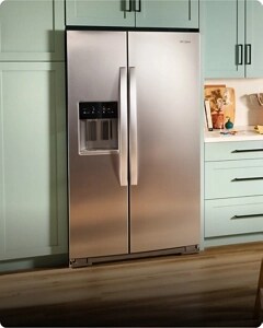 A stainless steel refrigerator installed between light green cabinets