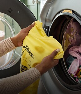 A person holding a shirt in front of a washer